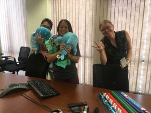 Two women and one man holding stuffed animals and giving a peace sign.